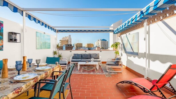 A rooftop terrace with a dining area, seating, and a view of the cityscape.