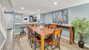 A dining area with a wooden table and chairs, a kitchen in the background, and a large painting on the wall. - Relaxing Oceanfront Escape w/ 2 Bedrooms & Fenced-in Backyard (Hilton Head Island)