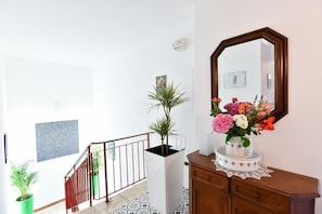 Staircase leads to an upper level, with a dresser, mirror, and potted plant below.