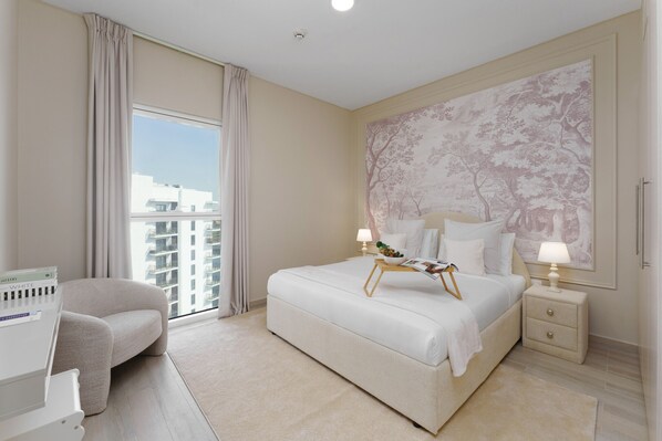A modern hotel room with a large bed, a bedside table with a lamp, a small side table, a window with curtains, and a large floral wall mural.