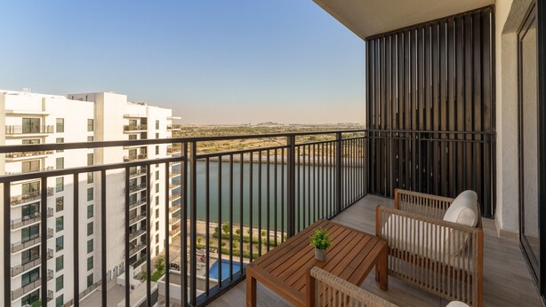 Un balcon avec une table et des chaises en bois, une vue sur une étendue d’eau et les bâtiments environnants.