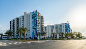 Un immeuble moderne à plusieurs étages, doté de balcons, de palmiers et surplombant un ciel dégagé.
