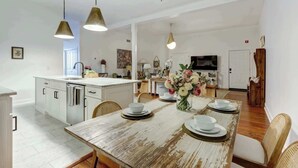 A spacious kitchen with a central island, pendant lighting, and a dining area with a rustic wooden table set for four. - A State of Mind, Modern | Historic | Central (Savannah)