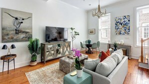 Ein Wohnzimmer mit Sofa, Fernseher, Esstisch und Stühlen.