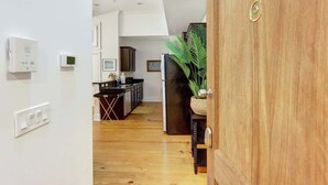 Ein Flur, der zu einer Küche mit Holzboden, einem Kühlschrank und einem Blumentopf führt.