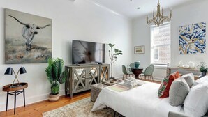 Ein modernes Schlafzimmer mit Bett, Fernseher, einer Chandelierleuchte, Kunstwerken und einem Essbereich.