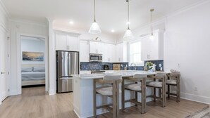 Una cocina moderna con armarios blancos, electrodomésticos de acero inoxidable y una isla central con taburetes de bar.
