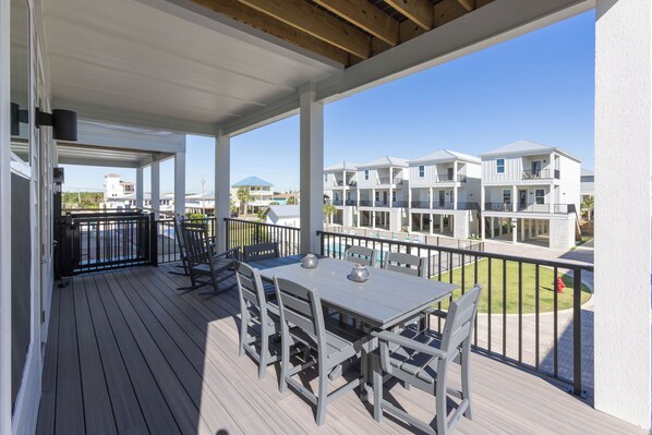 A covered outdoor deck with a table and chairs, overlooking a residential area with multiple-story buildings.