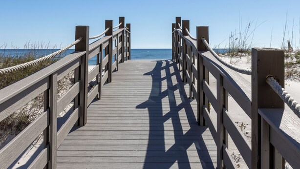 Una pasarela de madera que conduce a la playa, con barandillas a ambos lados.