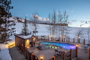 Uma área de piscina com deck de madeira, rodeada por uma cerca, com vista para uma montanha nevada.
