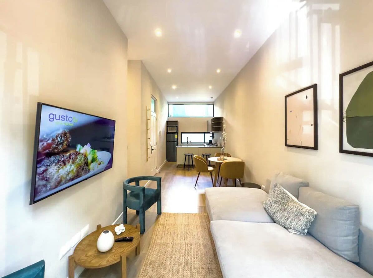 Een moderne woonkamer met een flatscreen televisie, een bank, een salontafel en een eethoek met stoelen en een kleine tafel.