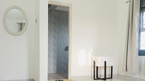 A modern hotel room with a large bed, a small table, a mirror, and a door leading to a bathroom. - 1 Bedroom Apartment Palm-View Balcony Entebbe (Nkumba)
