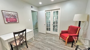 Una habitación con un escritorio, una silla roja, una mesa de vidrio y una puerta que da a otra habitación.