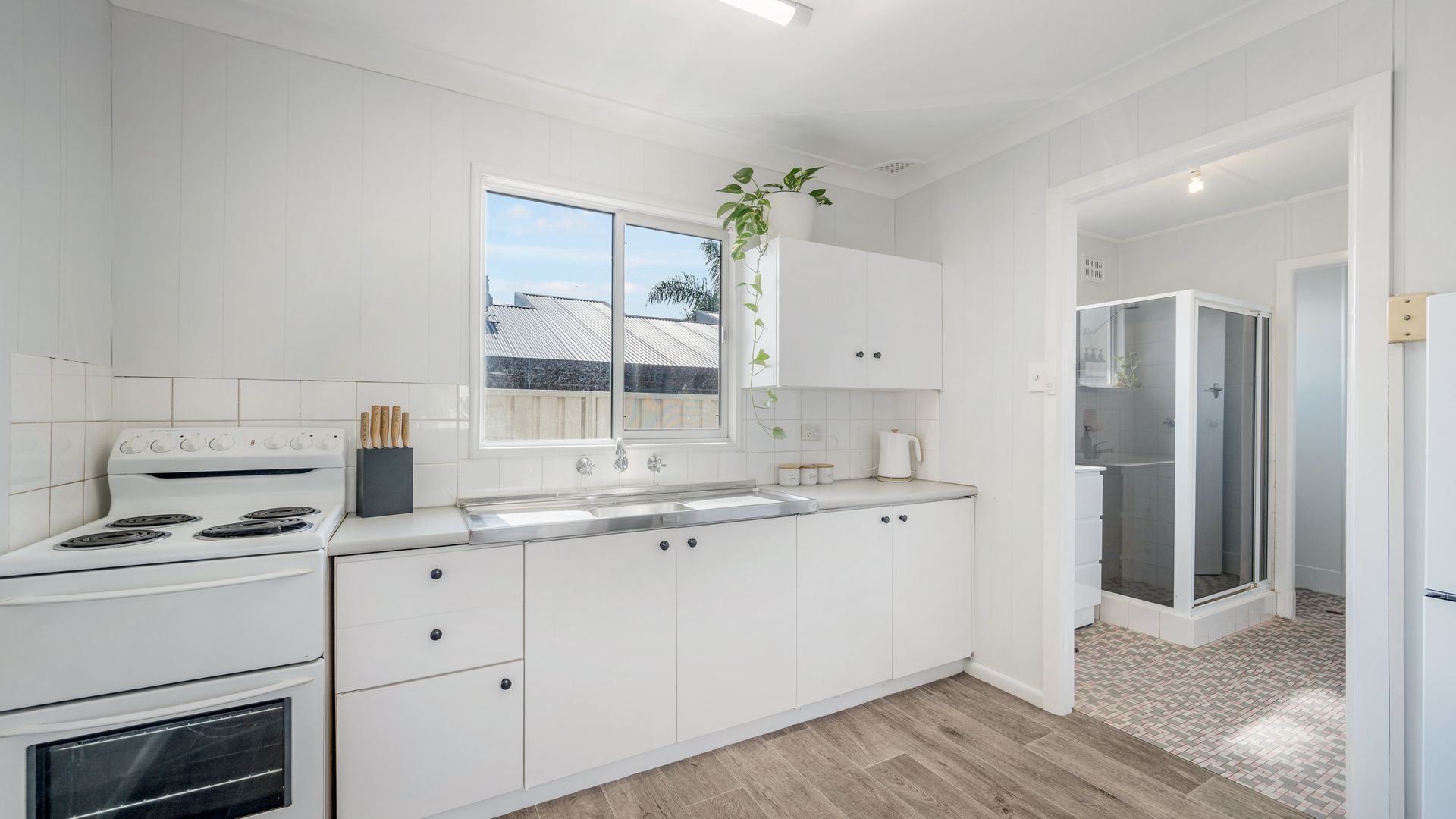 A modern kitchen with white cabinetry, a stove, and a sink. There is a window above the sink and a plant on the countertop.
