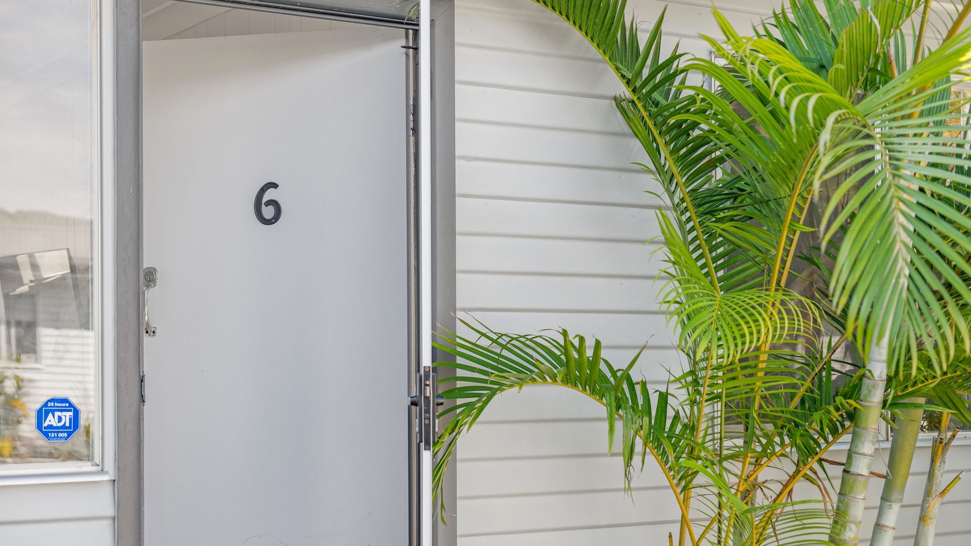 A white door with the number 6, a 24-hour ADT security sign, and a potted plant with green foliage.