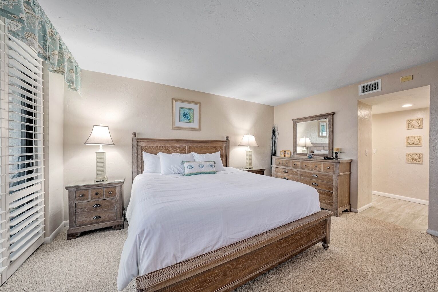 A bedroom with a large bed, wooden headboard, two bedside tables with lamps, a dresser, and a mirror.