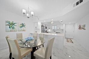 Una cocina moderna con armarios blancos, una isla central y un comedor con mesa y sillas de vidrio.