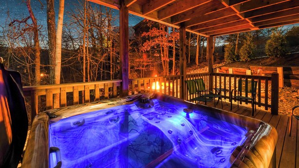 Ein Whirlpool mit Holzterrasse und Holzgeländer, umgeben von Bäumen und einem Nachthimmel.
