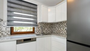 A modern kitchen with white cabinets, a stainless steel sink, and a window with patterned blinds. - Modern 2-Bedroom Apartment for up to 6 persons. (Orebic)