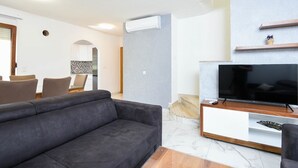 A modern living room with a grey sofa, a flat-screen TV on a wooden stand, and a dining area with chairs and a tiled backsplash. - Modern 2-Bedroom Apartment for up to 6 persons. (Orebic)