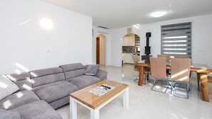 Een moderne woonkamer met een grijze modulaire bank, een houten salontafel en een eetgedeelte met een houten tafel en stoelen.
