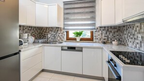 Een moderne keuken met witte kasten, een geïntegreerde vaatwasser, een fornuis en een raam met uitzicht op de omgeving.