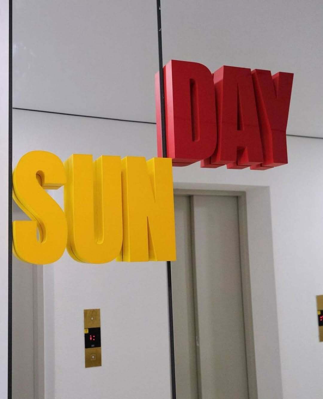 A wall with large, bold letters spelling "SUN" and "DAY" in yellow and red respectively.