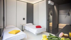 A modern hotel room with two beds, a small table with breakfast items, and a shower area.