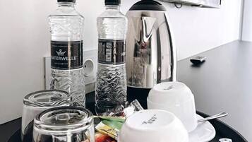 A hotel room with a breakfast tray containing two water bottles, a kettle, a white cup, a saucer, a glass, and a small plate with food.