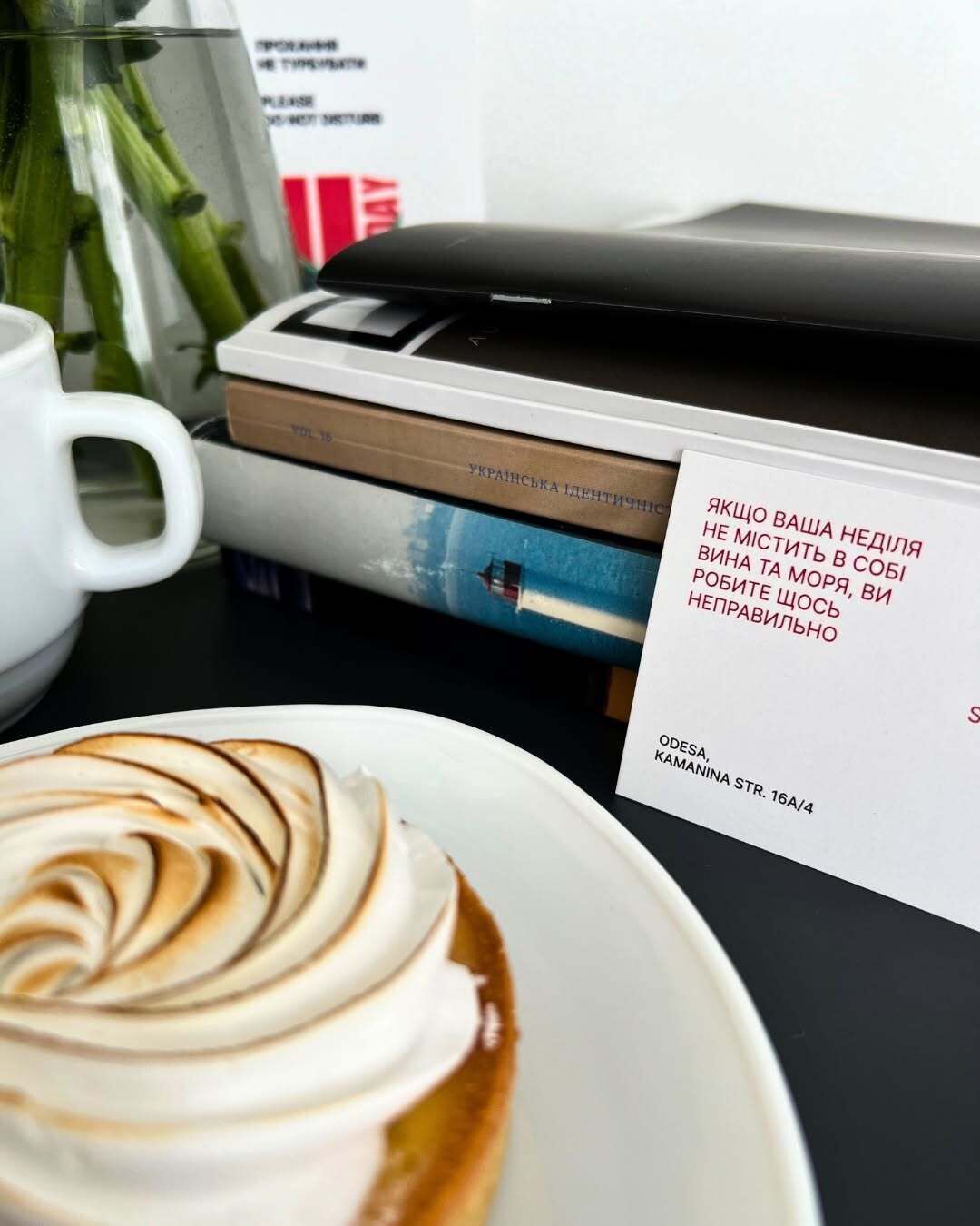 A cup of coffee with latte art on a plate, a stack of books, and a printed sign with text.