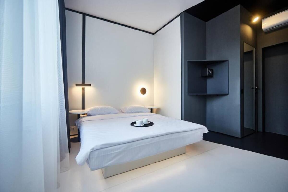 A modern bedroom with a large bed, bedside tables, a wall-mounted shelf, and a door.