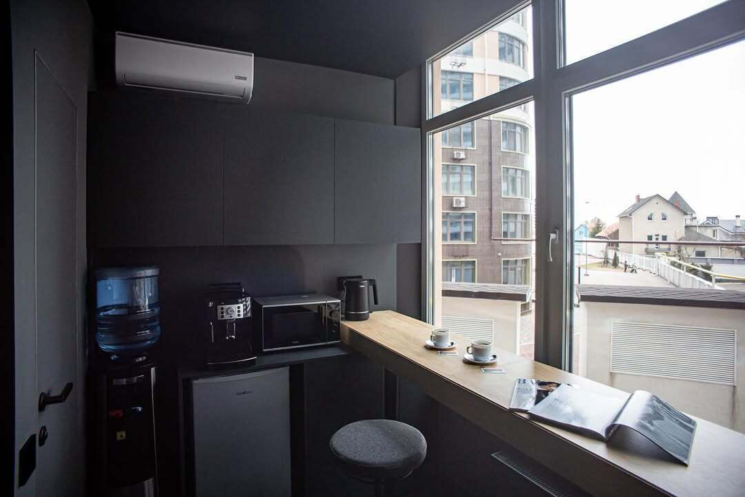 A compact kitchenette with a microwave, coffee maker, and water dispenser. A small stool is near the window, which offers a view of the cityscape.