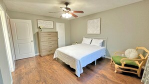 Un dormitorio con cama, cómoda, silla, ventilador de techo y obras de arte en las paredes.