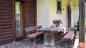 A rustic wooden cabin with a stone patio, a wooden bench, and a table with a vase of flowers. - Chalet Zala, Garden, Terace, EVcharger, Sauna, Jacuzzi  (Jesenice)