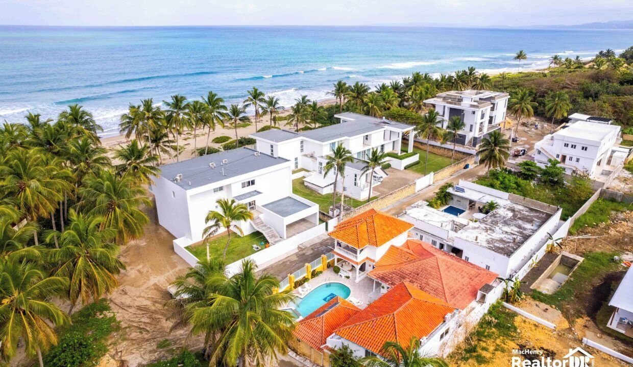 Un quartier résidentiel en bord de mer, avec des maisons modernes, une piscine et une plage en arrière-plan.