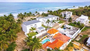 Zona residencial costera con casas modernas, una piscina y una playa al fondo.