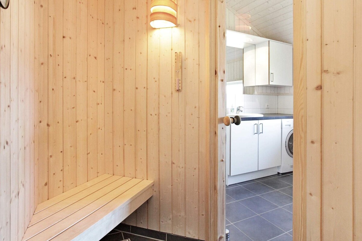 Ein Holz-Saunaraum mit einer Bank und einer Tür zu einer Küche mit weißen Schränken und einer Waschmaschine.