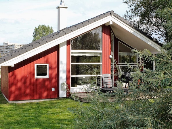 A red building with a sloped roof, large windows, and a small porch with chairs.