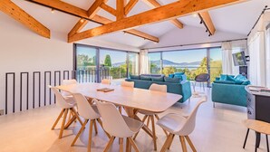 A modern interior with a wooden ceiling, a dining area with a table and chairs, a sofa, and a view of the outdoors.