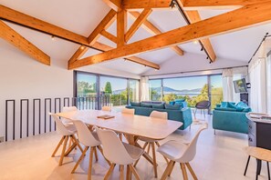 A modern interior with a wooden ceiling, a dining area with a table and chairs, a sofa, and a view of the outdoors.