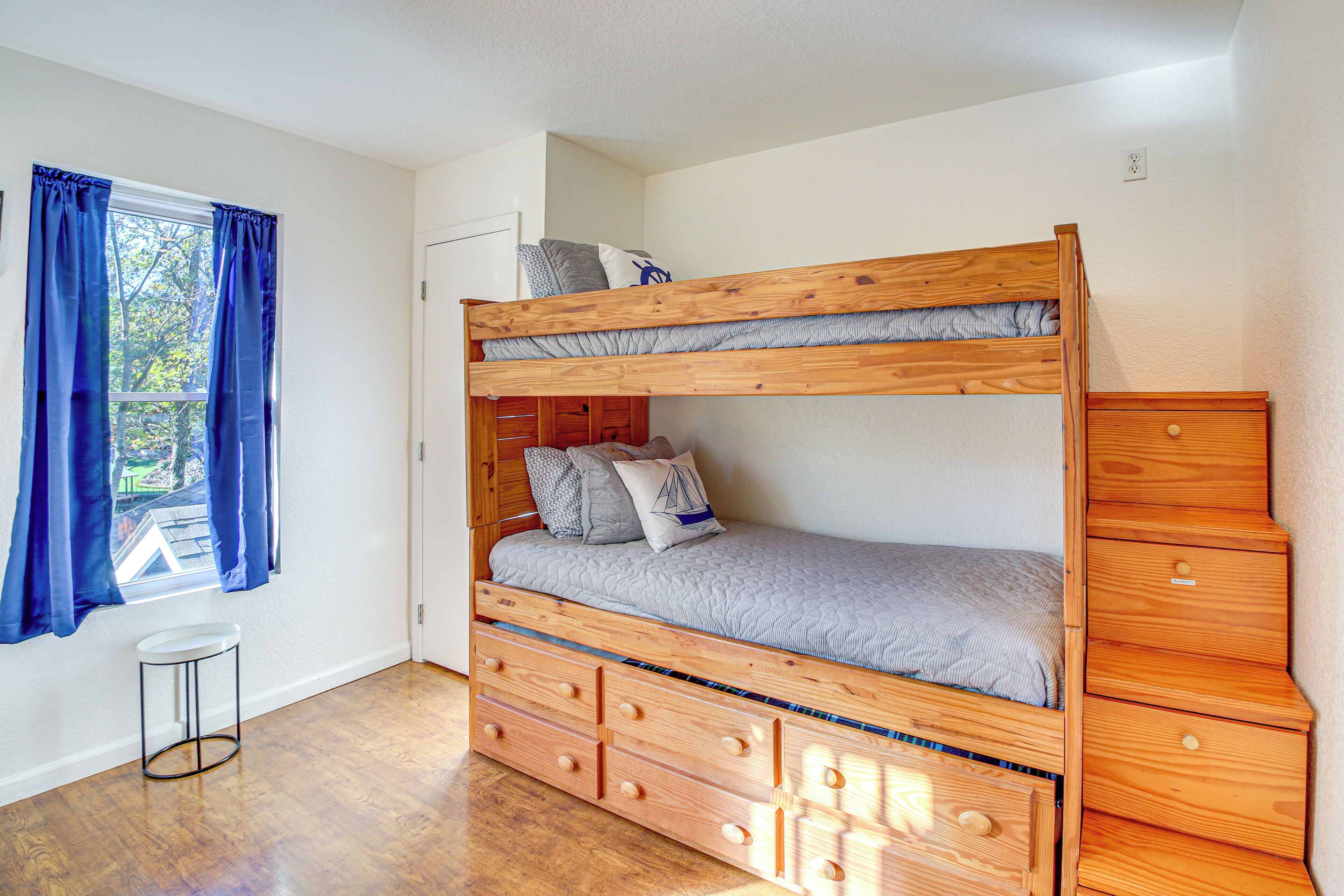 Un lit superposé avec une tête de lit en bois et des tiroirs, un petit tabouret et une commode avec un tiroir.