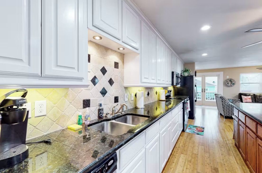 Una cocina moderna con armarios blancos, encimera de granito y pileta de acero inoxidable.