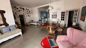 Un vaste espace de vie comprenant une table à manger, un canapé et un fauteuil rouge sur lequel est posé un ordinateur portable.