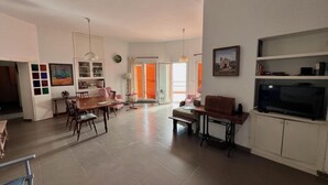 Un salon spacieux comprenant un coin repas, un téléviseur et une grande fenêtre dotée de volets orange.