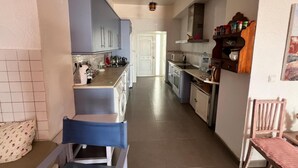 Une cuisine étroite avec des meubles de couleur bleue, un évier et une cuisinière. Il y a une chaise dans le coin et une porte qui donne sur une autre pièce.