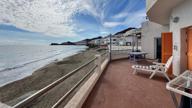 Un balcon avec vue sur la plage et l’océan, une table, des chaises et un étendoir.