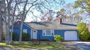 A single-story house with a blue exterior, a white garage door, and a front yard with trees and shrubs. - 3 bedroom home, quick drive to Northside Beaches (Dennis)