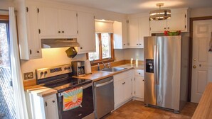 A kitchen with white cabinets, stainless steel appliances, a dishwasher, and a refrigerator. - 3 bedroom home, quick drive to Northside Beaches (Dennis)