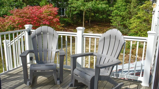 Two Adirondack chairs on a wooden deck with white railings, surrounded by greenery and trees. - 3 bedroom home, quick drive to Northside Beaches (Dennis)