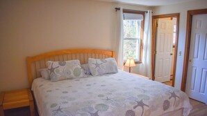 A bedroom with a wooden headboard, a bed with a starfish-patterned bedspread, a bedside table, and a window with a view of the outdoors. - 3 bedroom home, quick drive to Northside Beaches (Dennis)